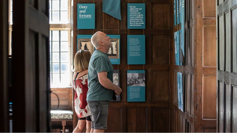 A man and a woman reading blue flags and interpretation panels hanging on the oak-panelled walls of the Great Parlour inside Avebury Manor